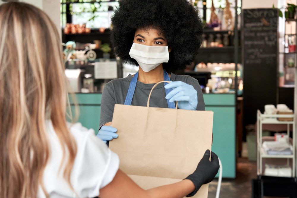 Woman handing purchased bag to customer, covid era with masks