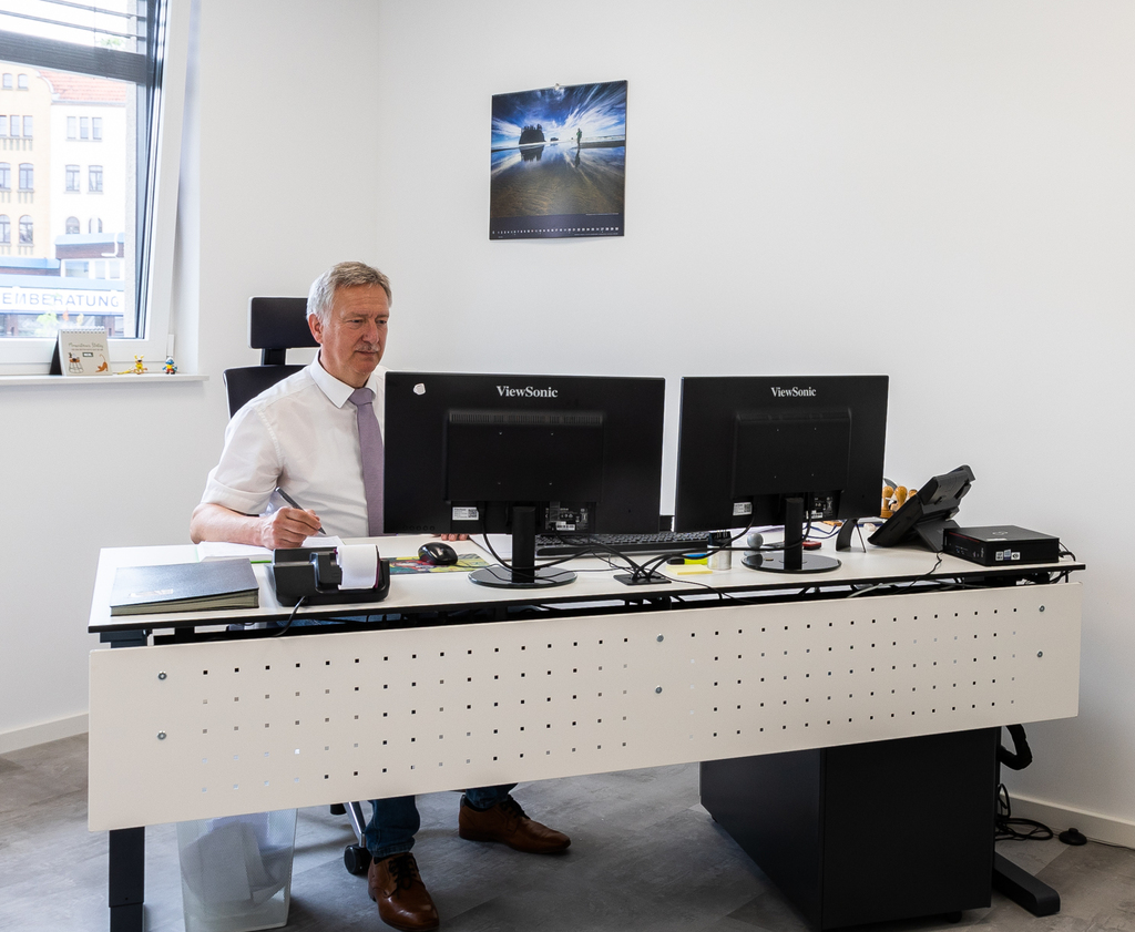 Jürgen Bliewert, der an einem Schreibtisch sitzt und etwas am Computer bearbeitet