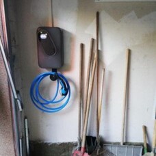 E-Auto-Ladestation mit blauem Kabel an Garagenwand, daneben Gartengeräte.