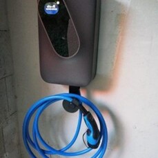 Wandmontierte E-Auto-Ladestation mit aufgewickeltem blauem Ladekabel.