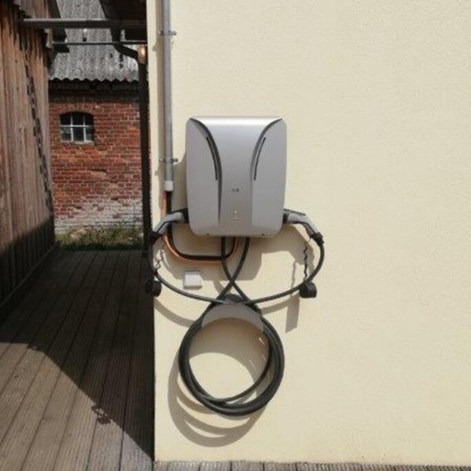 E-Auto-Ladestation mit aufgewickeltem Kabel an einer Hauswand.