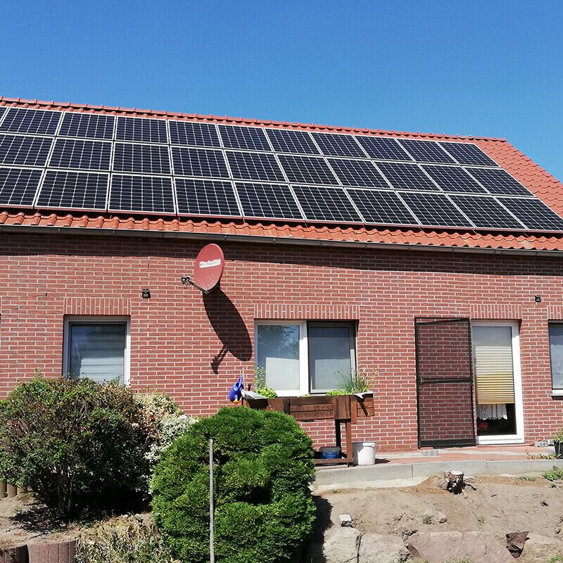 Einfamilienhaus aus rotem Backstein mit mehreren Solarpaneelen auf dem Dach, im Vordergrund gepflegter Vorgarten.