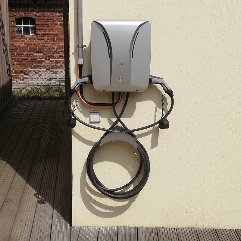 Wandladestation für Elektroautos mit ordentlich aufgewickeltem Kabel an einer hellen Hauswand.