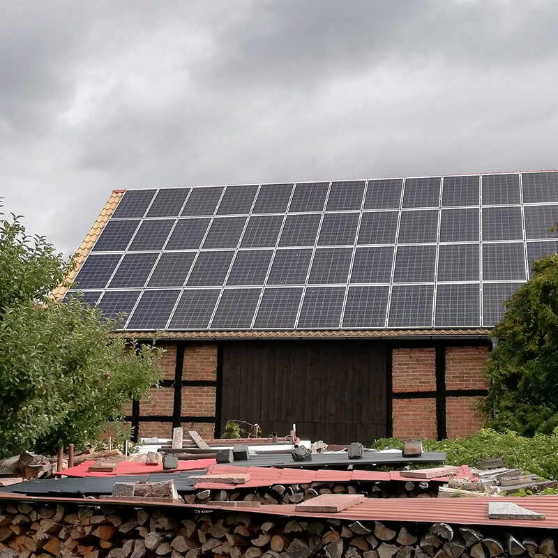 Holzverkleidetes Gebäude, vermutlich eine Scheune, mit großem Solarpaneel-Feld auf dem Dach.