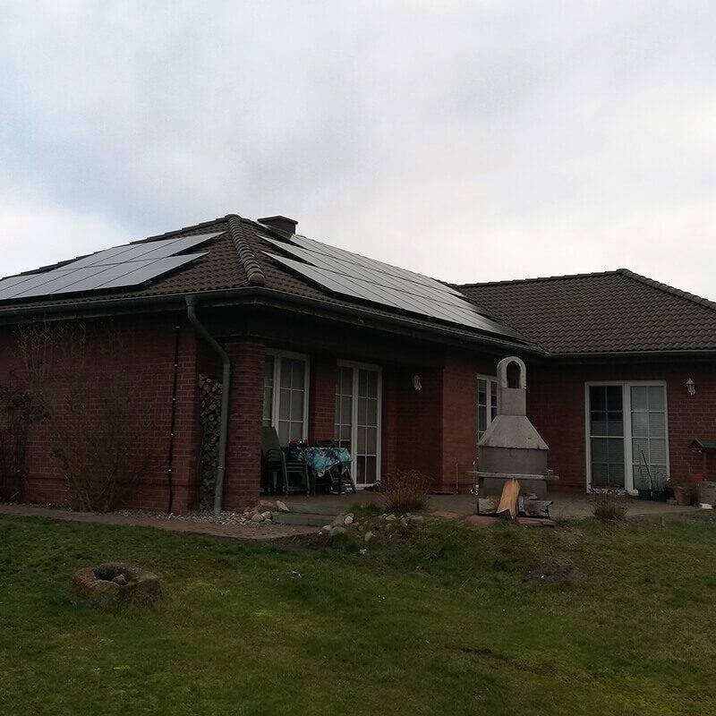 Freistehendes Haus aus rotem Backstein mit großflächiger Photovoltaikanlage auf dem schwarzen Schrägdach.