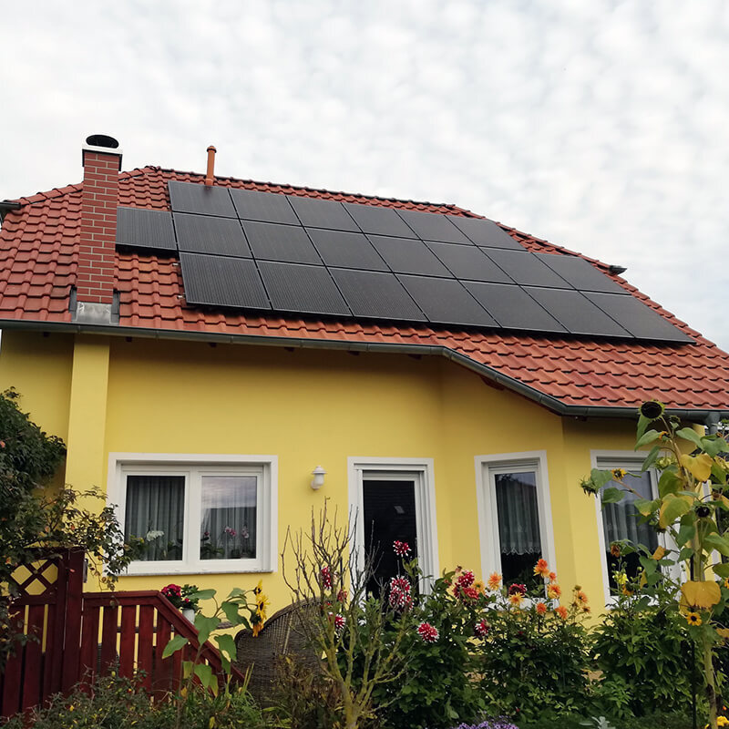 Einfamilienhaus mit gelber Fassade und rotem Ziegeldach, auf dem mehrere Solarpaneele installiert sind.